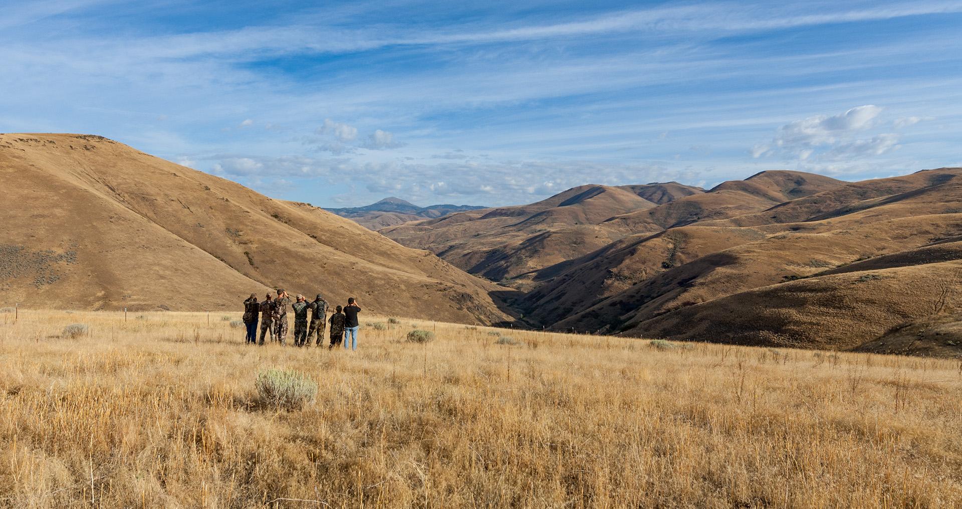 一群人站在田野里，用双筒望远镜眺望山谷